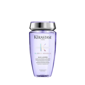 A bottle of Kérastase Paris Blond Absolu Bain Lumière shampoo with a silver cap, designed for lightened or highlighted hair, exemplifies premium hair care against a plain white background. | Blush Salon Collective - Fargo, ND