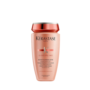A bottle of Kérastase Discipline Bain Fluidealiste shampoo with a peach and rose gold design, elegantly showcased against a white background. | Blush Salon Collective - Fargo, ND