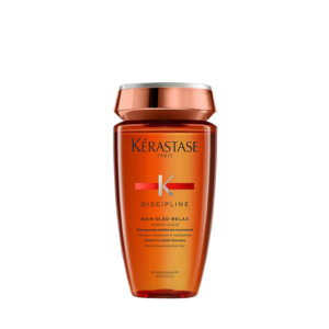 A bottle of Kérastase Discipline Bain Oléo-Relax shampoo, a premium hair care essential, with an orange and gold label, shown upright against a plain white background. | Blush Salon Collective - Fargo, ND