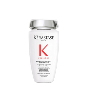 White bottle of Kérastase Première Bain Décalcifiant Réparateur shampoo with a silver cap, featuring bold black and red text highlighting “Reparateur” and “Première Bain Décalcifiant” on the front, set against a plain white background. | Blush Salon Collective - Fargo, ND